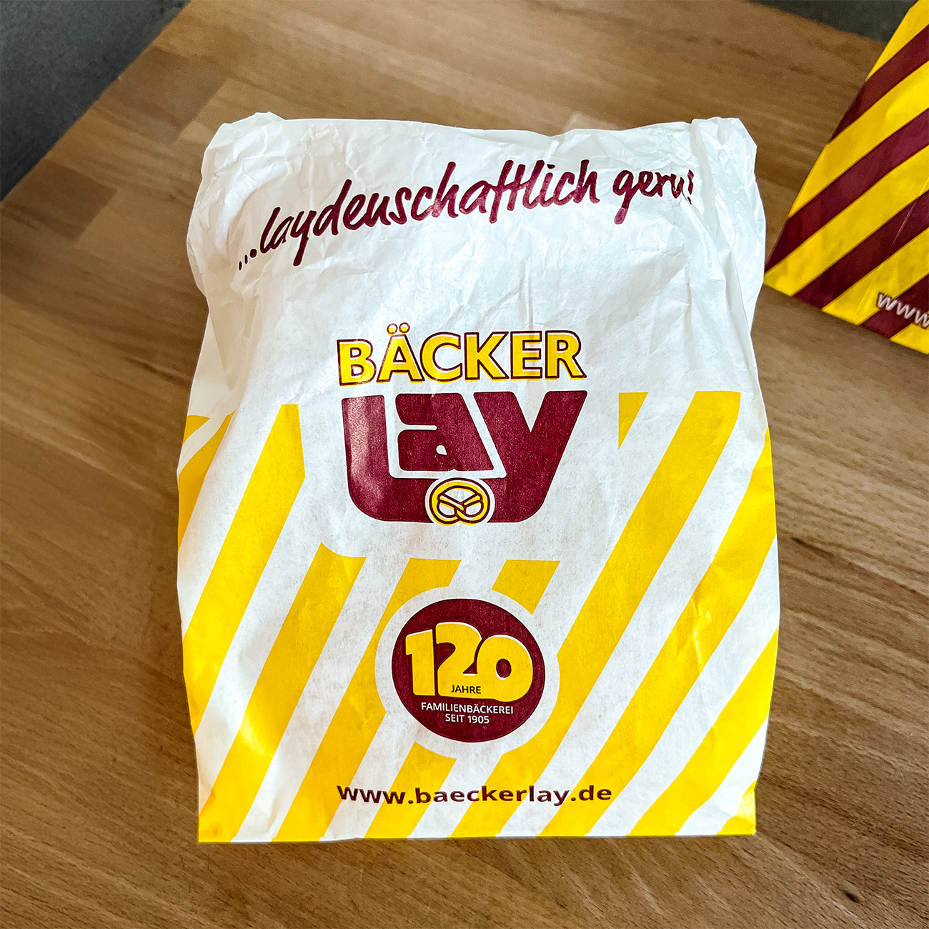 Einzelne Jubiläumstüte der Bäckerei Lay im neuen Design mit dem 120-Jahre-Signet und gelb-weißen Streifen – gestaltet von Frau Wolf im Rahmen des Jubiläumsauftritts.“
